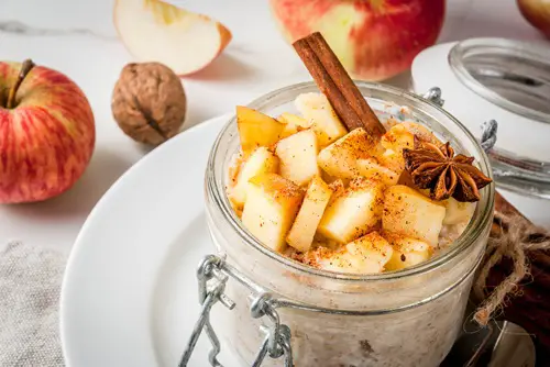 Healthy vegan food. Dietary breakfast or snack. Apple pie overnight oats, with apples, yogurt, cinnamon, spices, walnuts. In a glass, on a white marble table. Copy space