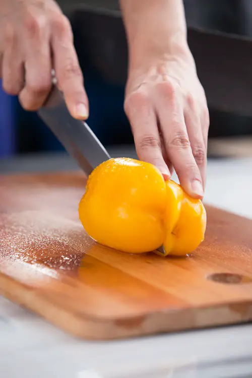 knife-is-cutting-into-yellow-bell-pepper-cutting-board