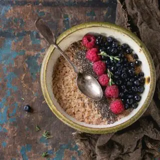 Bowl of oatmeal porridge with blueberries, raspberries and chia seeds, served with sackcloth rag and vintage spoon over old wood textured background. Rustic breakfast theme. Top view, space for text