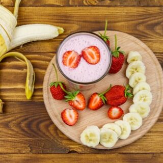 Glass of fresh smoothie of strawberry and banana on a wooden table. Top view