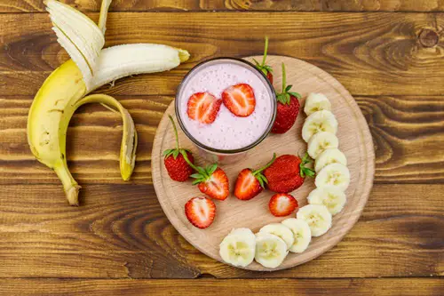 Glass of fresh smoothie of strawberry and banana on a wooden table. Top view