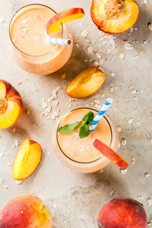 Healthy eating. Breakfast, snack. Drink smoothies from fresh peach, milk (yogurt) and oatmeal, decorated with mint leaves, with striped straws. On a light stone table. Copy space top view