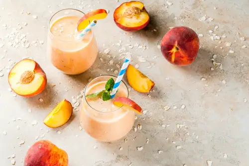 Healthy eating. Breakfast, snack. Drink smoothies from fresh peach, milk (yogurt) and oatmeal, decorated with mint leaves, with striped straws. On a light stone table. Copy space