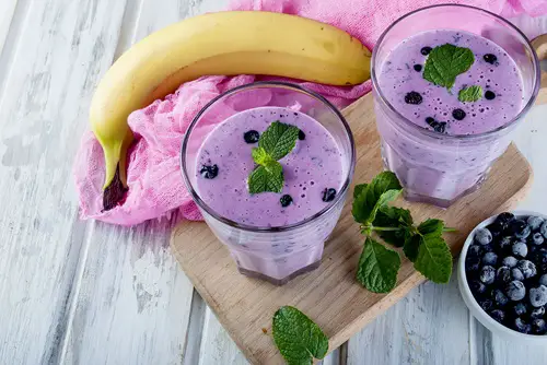 Refreshing Summer purple  smoothie or milkshake with mint, yogurt and blueberries. in glass, on wooden table, copy space, top view Blueberry Banana Smoothie